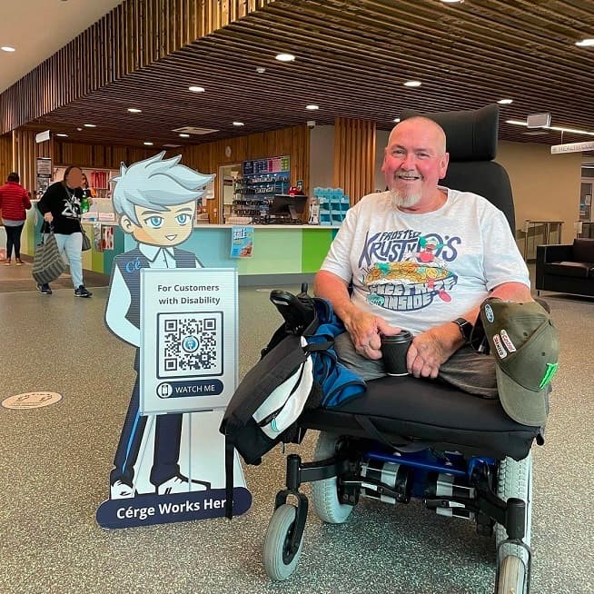 A man kneels beside a cartoon cutout with a QR sign at a pool facility. A man kneels beside a cartoon cutout with a QR sign at a pool facility.