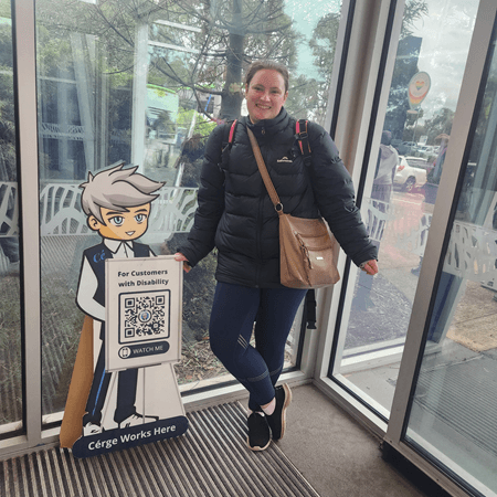 A woman in a black jacket stands beside a Cérge cartoon cutout with a QR sign. A woman in a black jacket stands beside a Cérge cartoon cutout with a QR sign.